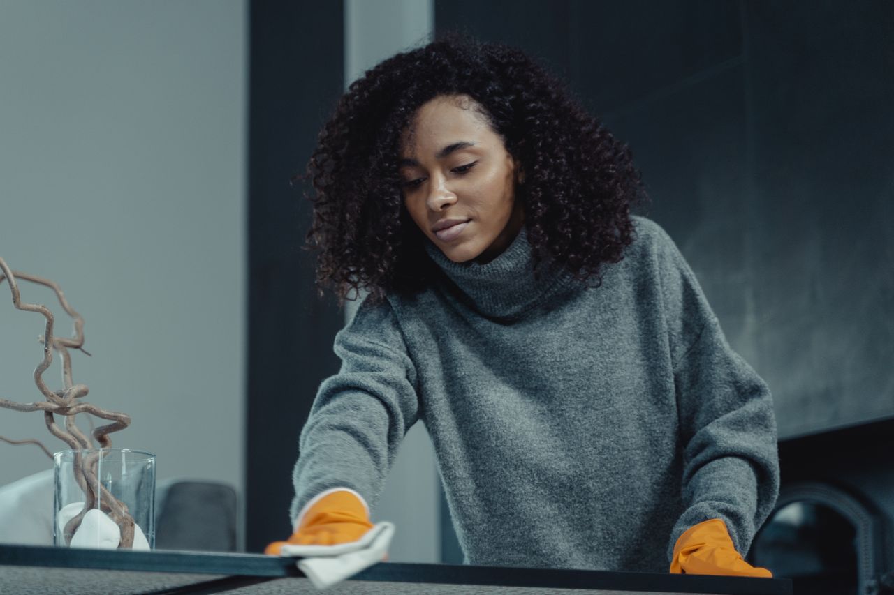 why-choose-us-03 A woman in a gray sweater wipes a table with care, showcasing home cleaning in comfort.